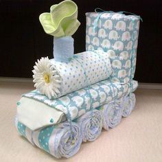 a stack of rolled up baby blankets next to a vase with a flower in it