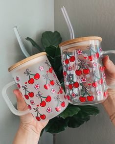 two coffee mugs with cherries on them are being held by someone's hand