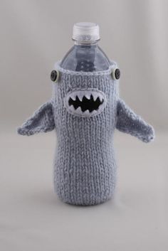 a knitted water bottle cover with a shark face on the front, and a black mouth