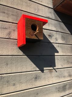 a red birdhouse hanging on the side of a gray wooden building with a window