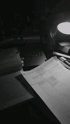 a desk with a laptop, pen and paper on it in the dark night time