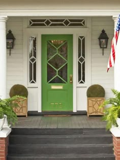 a green front door with two planters on the steps and an american flag hanging above it