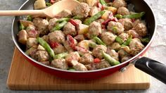 a pan filled with meat and vegetables on top of a cutting board next to a wooden spoon