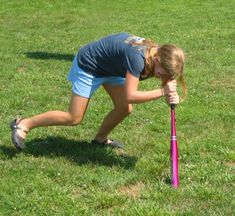 a woman bending over to pick up a purple baseball bat