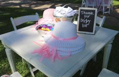 a white table topped with a pink hat next to a chalkboard