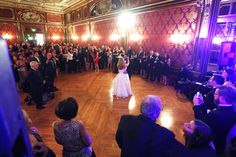 a woman in a white dress standing on top of a wooden floor next to a crowd