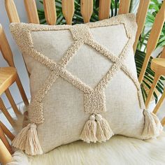 a pillow with tassels on it sitting on a chair next to a plant