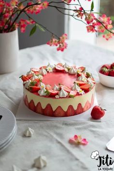 a cake with strawberries and whipped cream on top sitting on a table next to flowers