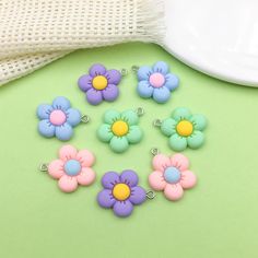 six flower charms sitting on top of a green table next to a white plate and cloth