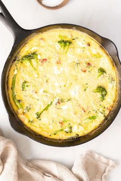 an omelet with broccoli and cheese in a skillet on a white surface