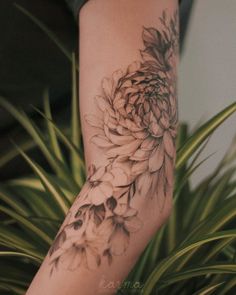 a woman's arm with a flower tattoo on it and a plant in the background