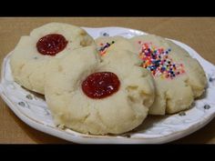 three cookies with sprinkles and jelly on a white plate next to each other