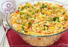 a glass bowl filled with pasta salad on top of a red place mat next to silverware