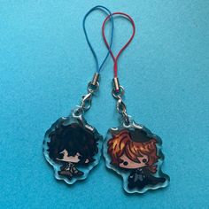 two little tags with anime characters on them sitting on a blue surface, one has a red cord