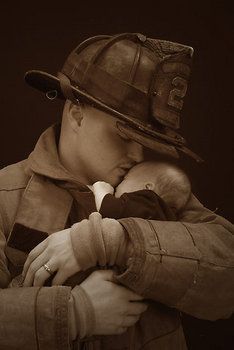 a man in a fireman's hat holding a baby on his lap and kissing him