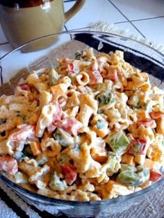 a glass bowl filled with pasta salad on top of a white tiled counter next to a cup