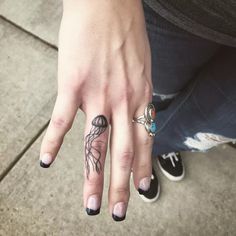 a woman's hand with tattoos on it and two rings in the middle of her fingers