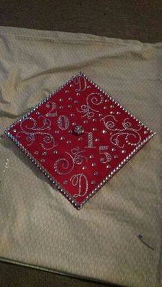 a red and white graduation cap with silver sequins on the bottom is sitting on a piece of cloth