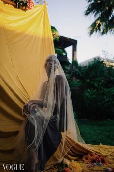 a woman is sitting on the ground with her veil over her head and flowers around her neck