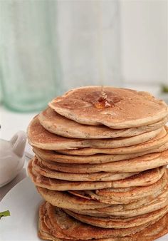 a stack of pancakes sitting on top of a white plate next to a tea pot