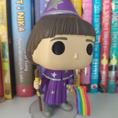 a purple wizard figurine holding a rainbow flag and standing in front of books