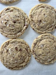 chocolate chip cookies with white flecks are arranged on a sheet of parchment paper