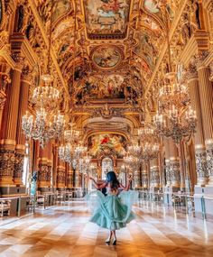 a woman in a blue dress is standing in an ornate room with chandeliers