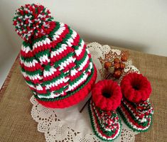 a knitted hat and booties are sitting on a doily next to a pair of slippers