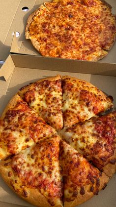 two pizzas sitting in boxes on top of a table with one slice missing from it