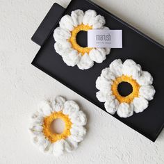 two crocheted flowers sitting on top of a black tray next to each other