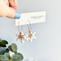 a pair of white flower earrings is being held up by a woman's hand