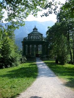 a gazebo sitting in the middle of a lush green forest next to a dirt road