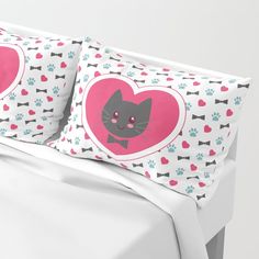 a bed with two pillows on top of it and a cat in a heart shaped pillow