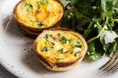 two mini quiches on a white plate next to a green leafy salad and fork