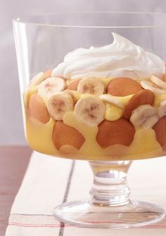 a dessert in a glass dish with bananas and whipped cream on top, sitting on a table