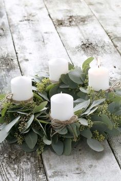 some white candles sitting on top of green leaves and greenery in front of a wooden table