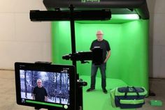 a man is standing in front of a green screen with a camera and laptop on it