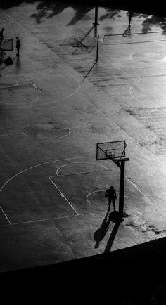 two people playing basketball on an outdoor court in the evening sun, with one person running towards the basket