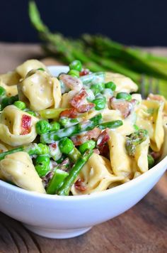 a white bowl filled with pasta and asparagus on top of a wooden table