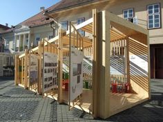 a wooden structure sitting on the side of a road next to tall buildings with windows