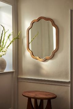 a mirror hanging on the wall next to a table and vase with flowers in it