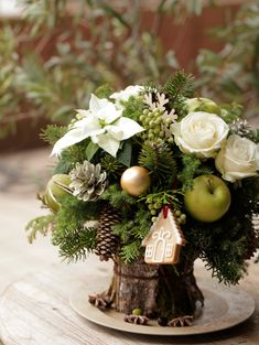 an arrangement of flowers, apples and greenery in a vase on a wooden table