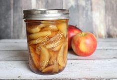 an apple cider with apples in it on a wooden table next to a mason jar