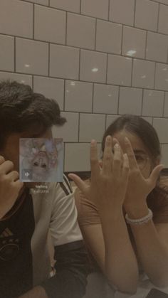 two people sitting next to each other in front of a mirror with their hands up