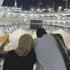 two people sitting in front of the ka'bah at night, looking out over the crowd