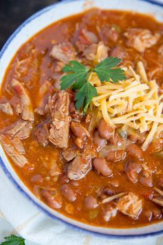 a white bowl filled with meat and beans covered in cheese on top of a napkin