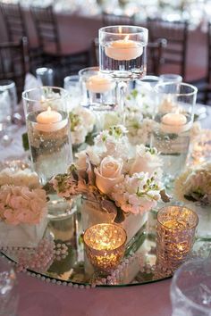 a table topped with lots of glass vases filled with flowers and candles