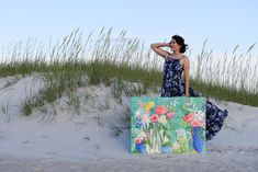 a woman is standing on the beach with a painting in front of her and grass behind her