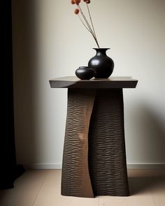 two black vases sitting on top of a wooden table next to each other in front of a white wall