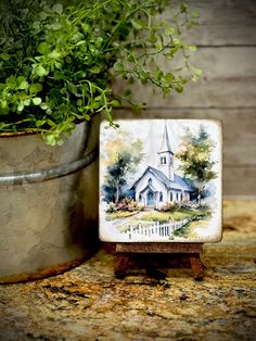 a small tile with a painting of a church on it next to a potted plant